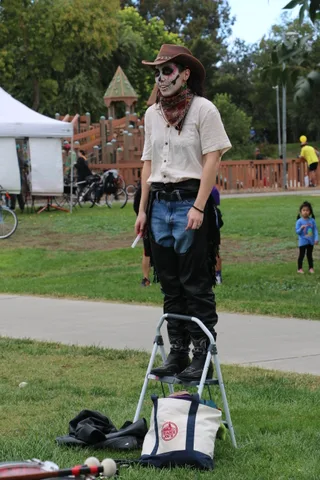 A man in cowboy hat and skeleton face paint walks alone near the playground.