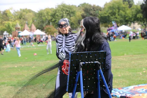 A woman in skeleton makeup holds flowers while another films with a tripod camera.