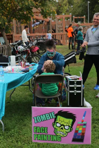 A child gets their face painted at a booth near the playground.