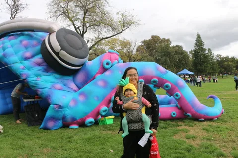A woman carries a costumed baby past the inflatable tentacle display.