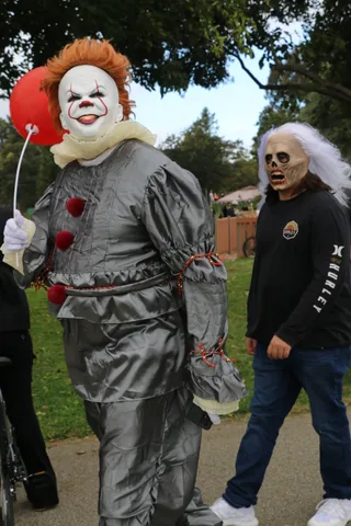 A vivid Pennywise-style clown costume with a red balloon draws the eye beside a skeleton-faced rider.