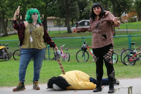 Two zombie performers stand near a costumed figure lying on the ground.