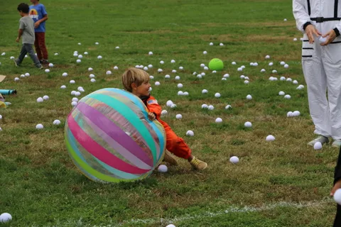 A large striped beach ball dominates the frame as a child runs behind it.