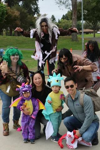 A family poses together, with two children dressed as a dragon and dinosaur.