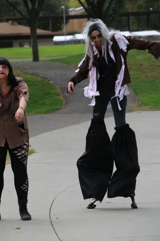 A stilt walker's legs and black robe are visible against the pavement.