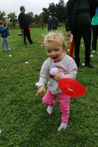 A toddler beams with delight while holding a striped foam pole in the grass.