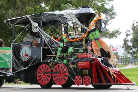 A Halloween-decorated black locomotive with red wheels sits in the park.