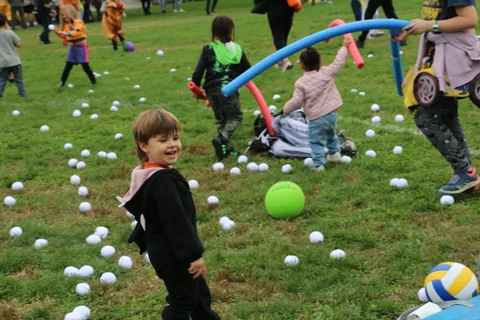 A boy reaches with a pool noodle while playing a ball game in the park.