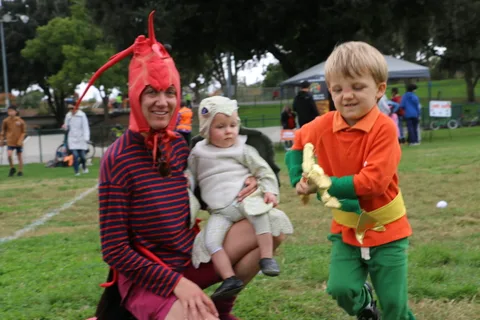 A boy dressed as Aquaman holds a trident near his costumed family.