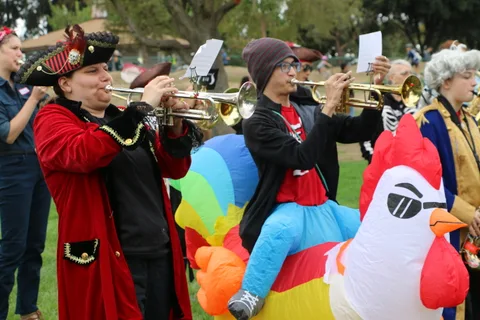 Trumpet players in pirate costume perform beside an inflatable chicken.