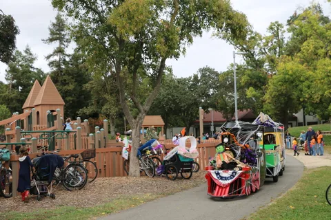 Children play at a castle-themed playground with decorated parade trains parked nearby.