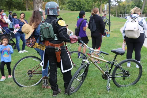 A rider in medieval armor stands with a bike as bystanders look on.