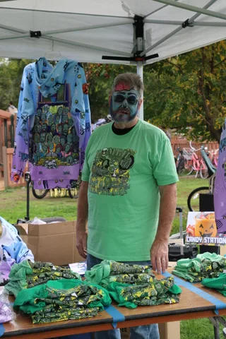 A vendor arranges folded green festival T-shirts on a table near boxes.