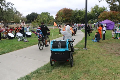 A wide view of riders with flags heading down the path past tents.