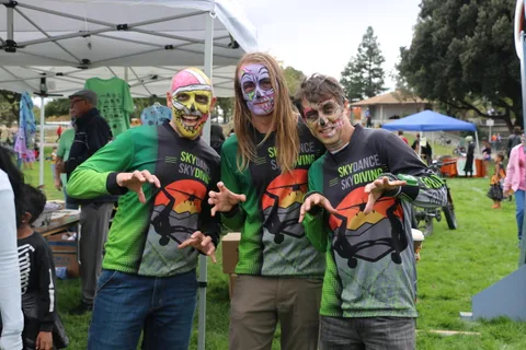 Three people in matching skydiving shirts and skull makeup pose together.