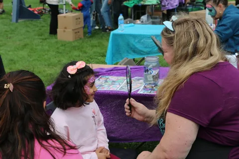 Children with festive face decorations gather near a decorated table at the festival.