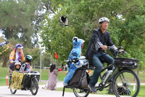 A family rides a decorated cargo bike along the park path with a red flag flying.