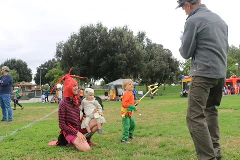 Two children in costume play in the grass as a man watches from a distance.