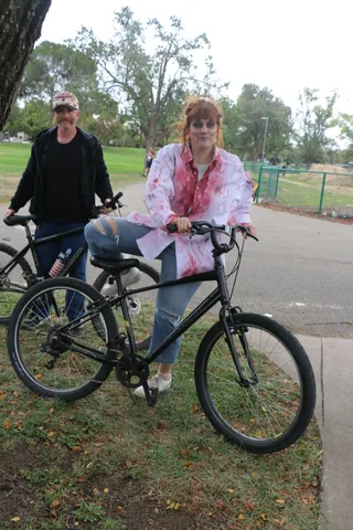 A man and a bloodied zombie bride pose together with their bikes on the path.
