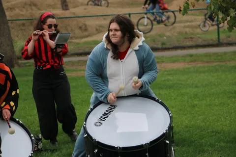 A drummer smiles while playing a large floor tom as someone films her.
