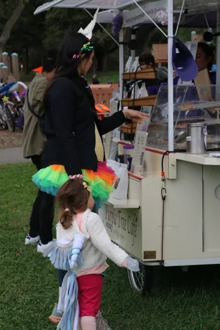 Two girls in colorful costumes walk together near a cafe cart.