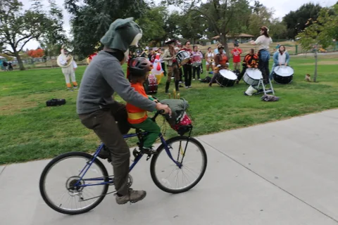 A rider in a green hood pedals along the path with a child in tow.