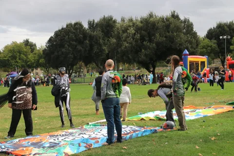 People in Halloween costumes walk across a park with bounce houses in the distance.