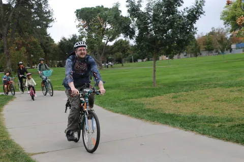 A man in a denim jacket rides alone down the sparse path.