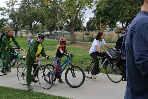 A line of cyclists, including a child, rides along the park path.