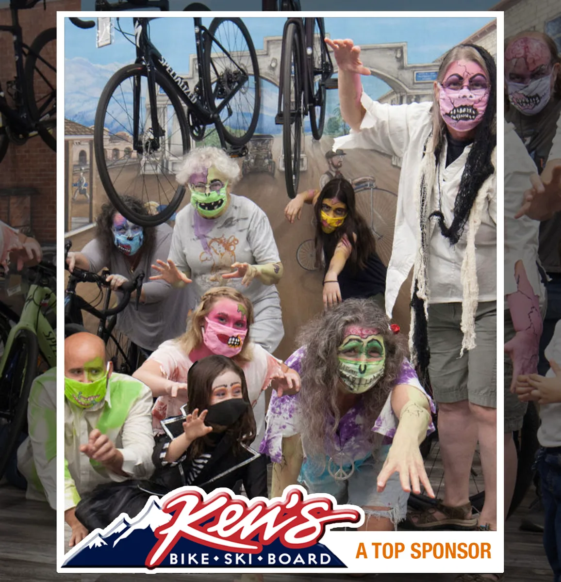 A group of zombie-costumed people crawl toward the camera in front of a Ken's Bike Ski Board banner.
