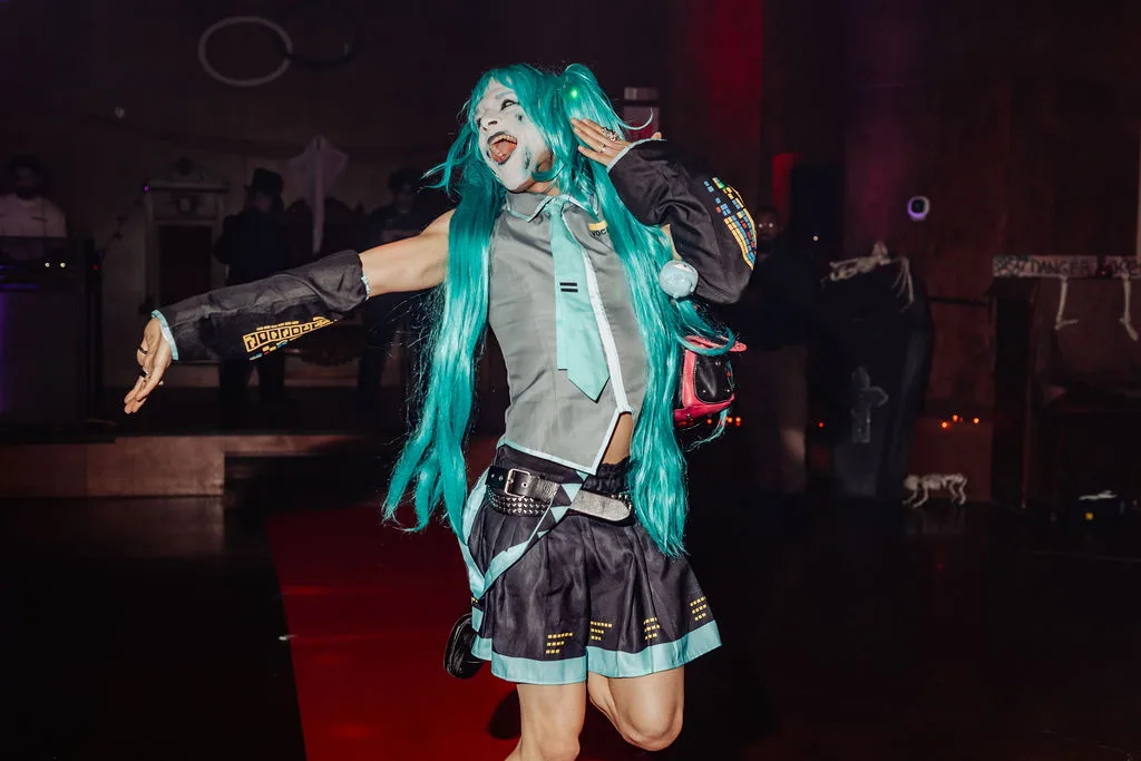 A guest in a teal wig and ghostly makeup laughs on the Zombie Ball red carpet.