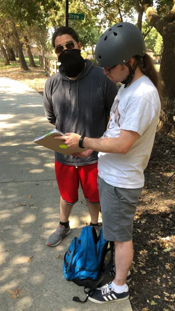 Two men look over a clipboard outdoors.