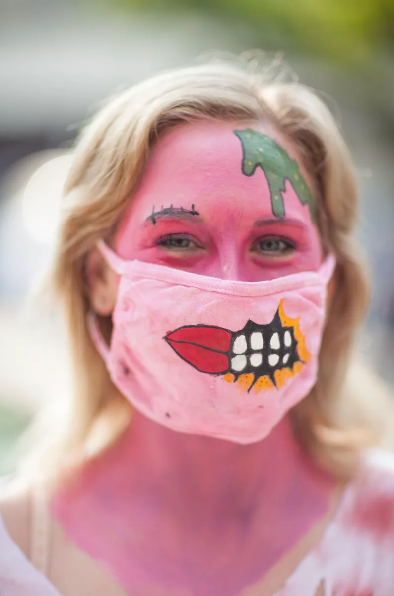 A woman shows off pink zombie face paint with a painted skull mouth design.