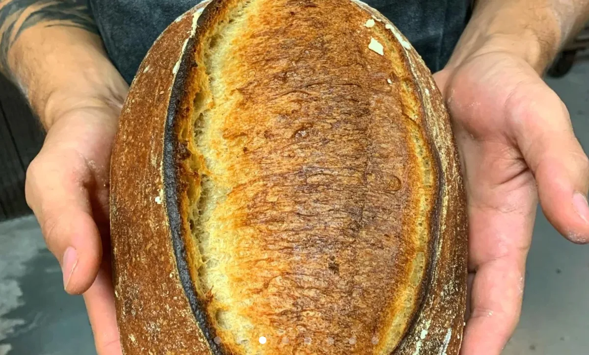 A hand holds a freshly baked round sourdough loaf.