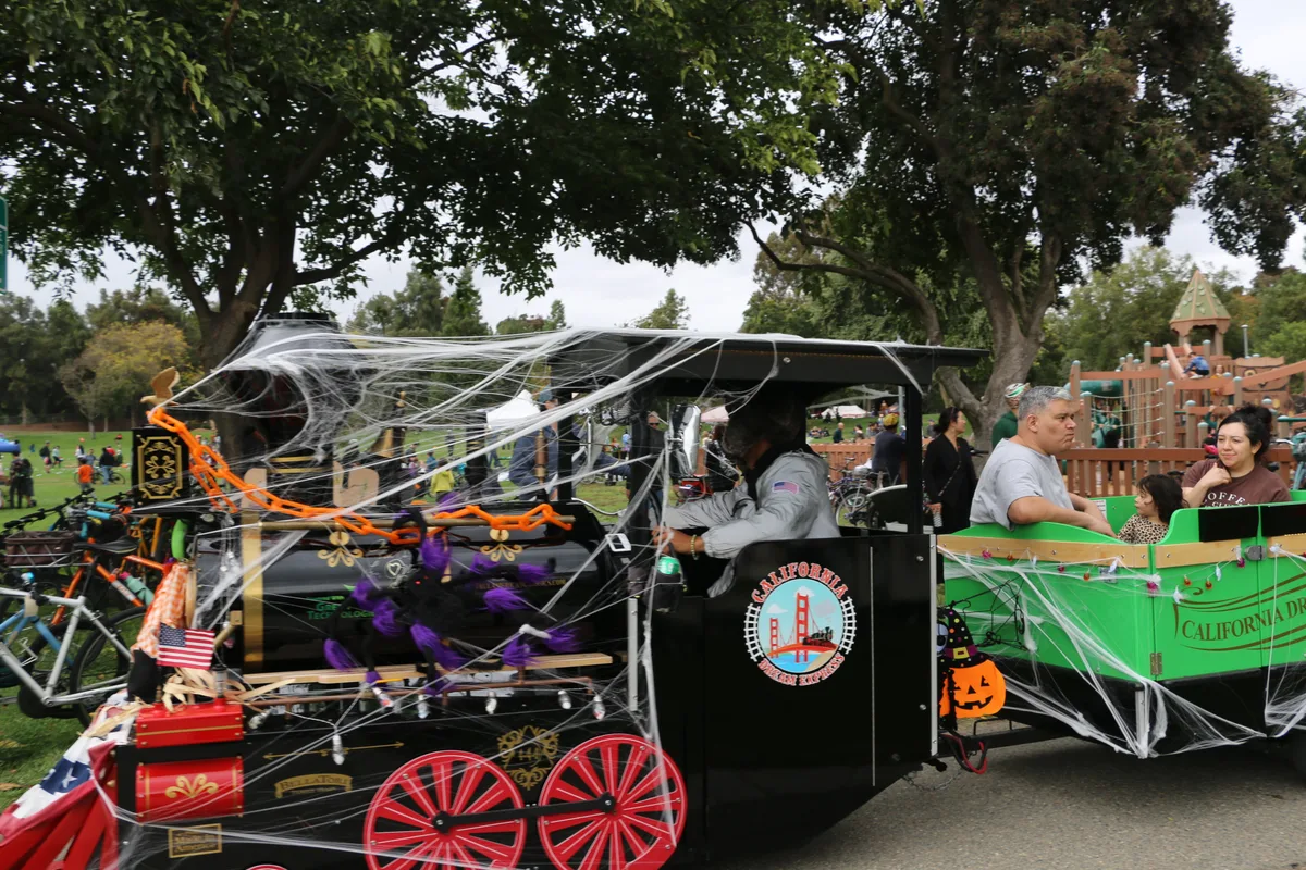 A cobweb-draped carriage float with red wheels sits parked in the park.