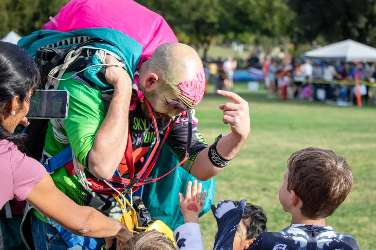 A man in zombie makeup clowns around with kids in the park.