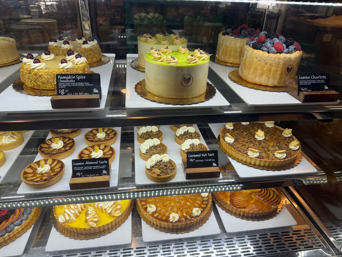 A bakery display case shows a row of decorated cakes.