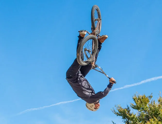 A BMX rider flips upside down high against a clear blue sky.