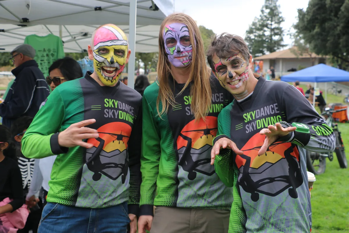 Three volunteers in skull face paint pose in their Skydance Skydiving festival shirts.