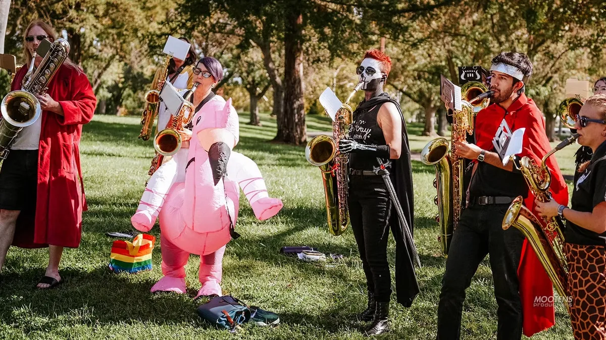 Musicians with saxophones perform beside a person in a pink flamingo costume.
