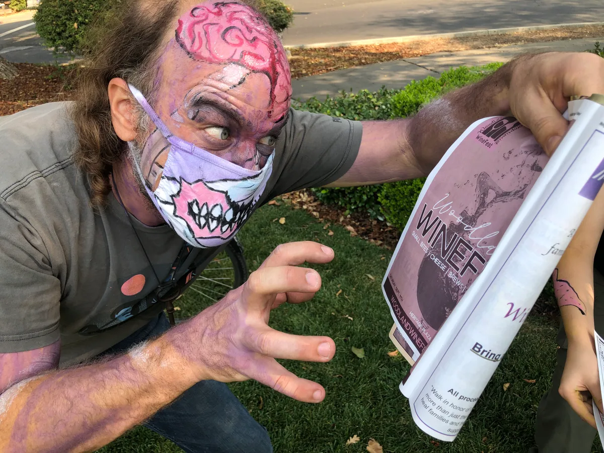 A man with exposed-brain face paint growls while holding a prop newspaper.
