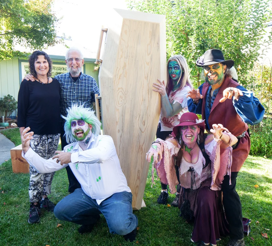 A costumed group holds up a blank wooden sign board outdoors.