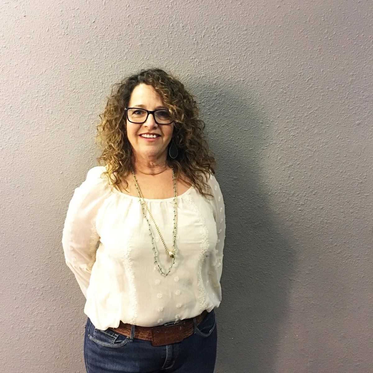 A woman smiles for a portrait against a plain wall.