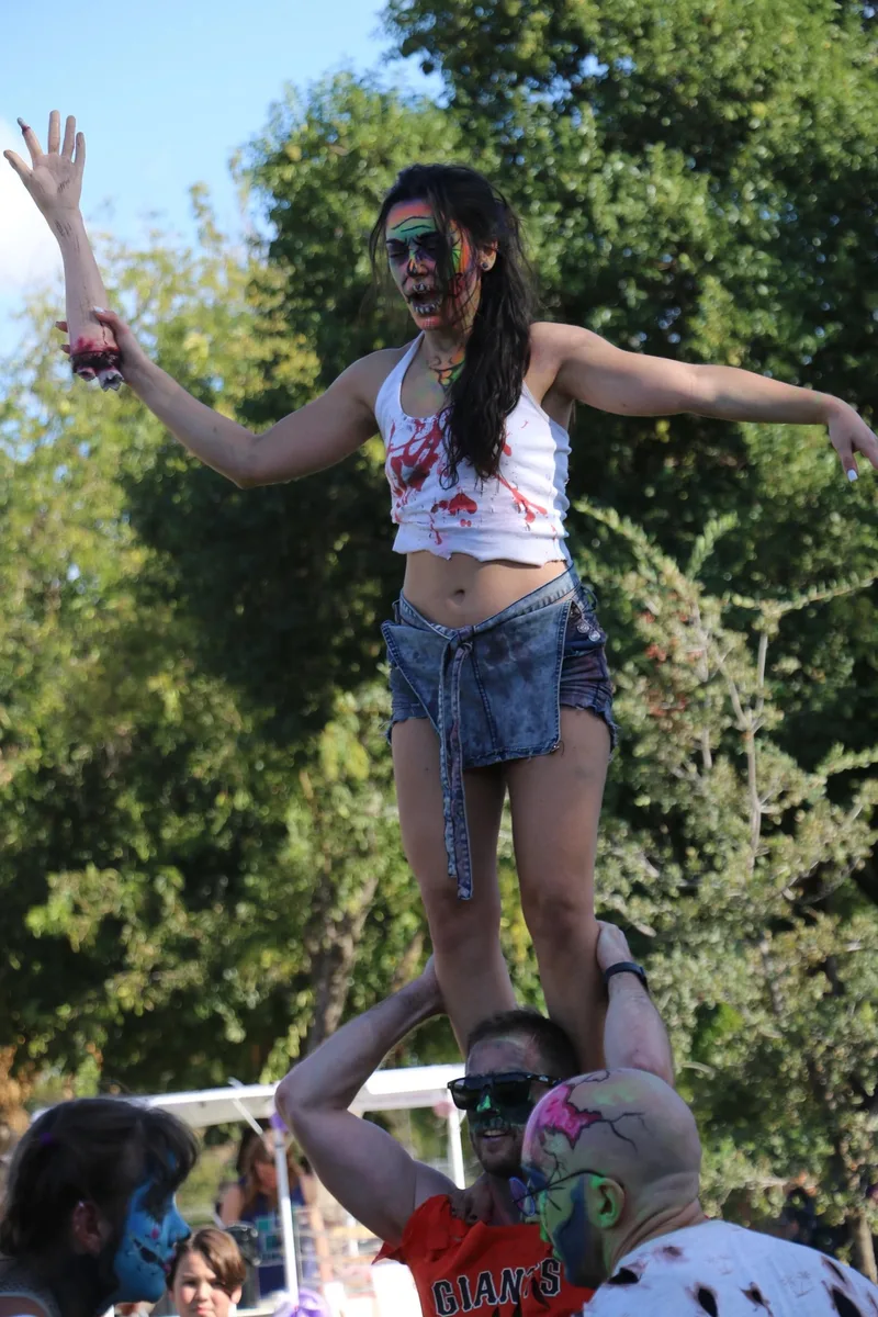 A performer holds a woman in a handstand pose during a park stunt show.
