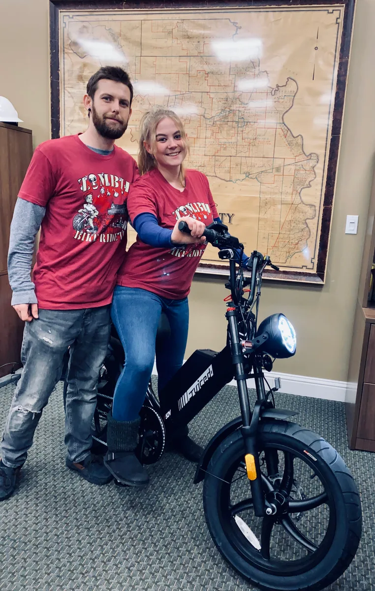 A couple poses with their bikes and a route map wearing Zombie Bike Ride jerseys.