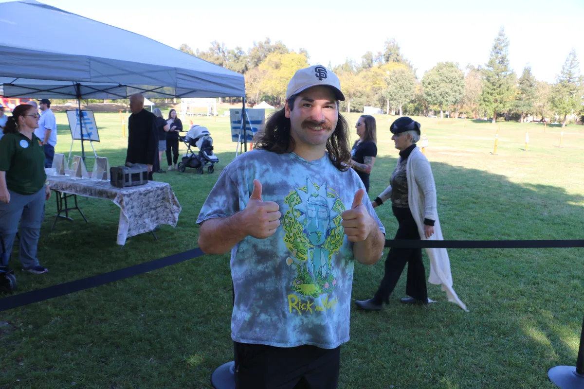 A man gives a thumbs up at the festival with a tent in the background.