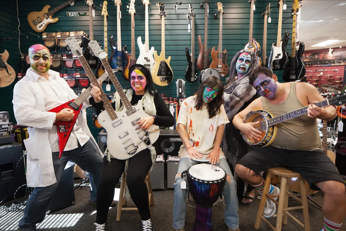 A costumed group poses with guitars and drums inside a music shop.
