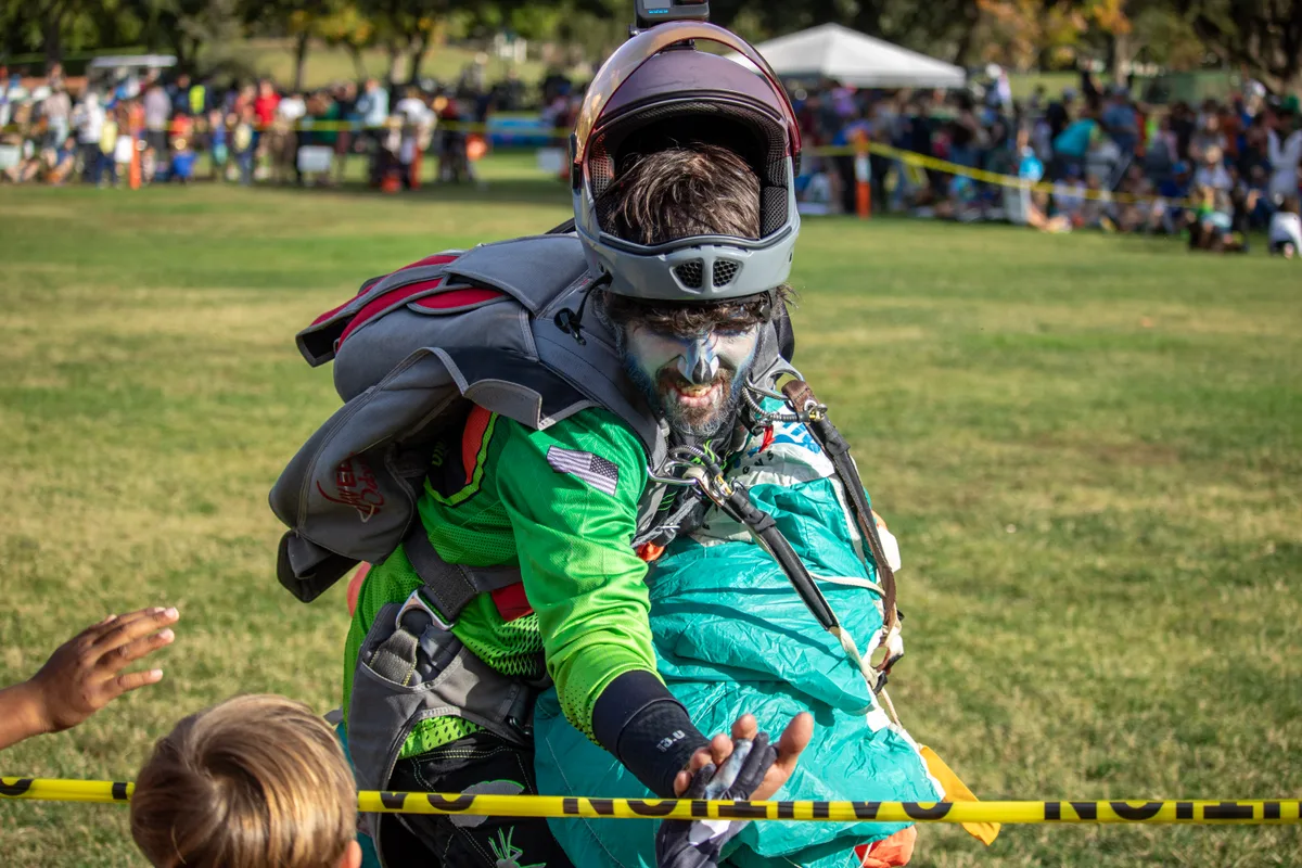 Two people sit on the grass near a skydiving helmet after a landing.