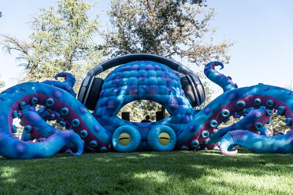 A blue inflatable bounce house shaped like an octopus sits on the grass.