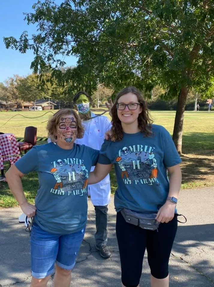 Two women wear matching Zombie Bike Parade shirts on the sidewalk.